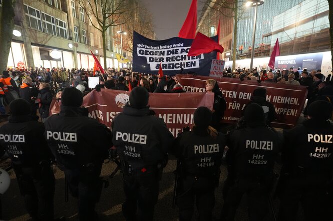 Vor einer Polizeikette stehen Menschen mit Transparenten wie "Gegen die Politik der Rechten und Reichen"