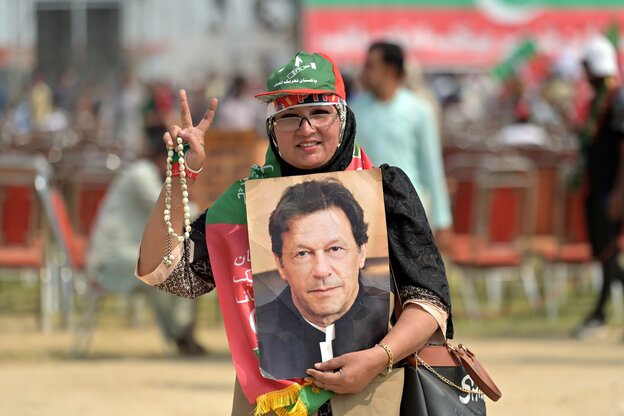 Eine Frau macht das Siegeszeichen und hält ein Foto von Imran Khan in den Händen