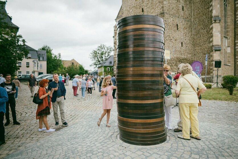 Blick auf die Kunstinstallation Coin Stack von Sean Scully vor der spätgotischen Kirche von Schneeberg. Sie zeigt einen ca. drei Meter hohen Stapel überdimensionierter Geldmünzen