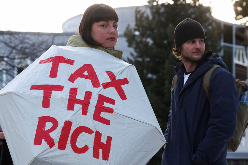 Eine Demonstrantin hält einen Regenschirm, auf dem steht "Tax the rich"