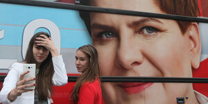 Mödchen fotografieren sich vor einem Wahlplakat der Partei Recht und Gerechtigkeit