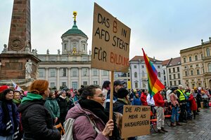 Menschen demonstrieren mit Regenbogenfahnen und Plakaten, auf einem steht 