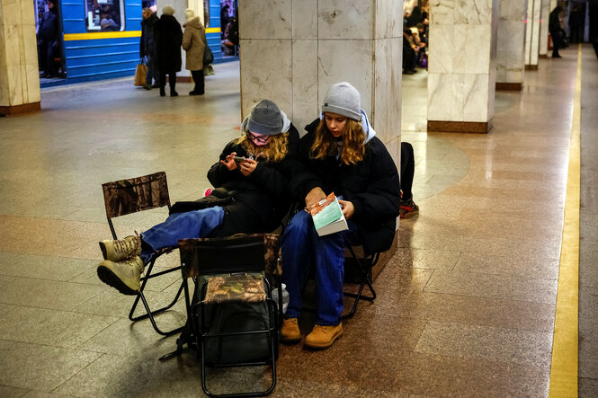 Zwei Frauen sitzen auf einem U-Bahnsteig, eine hat ein Smartphone in den Händen