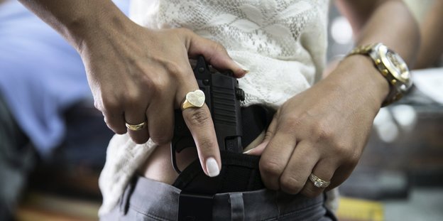 Eine Frau steckt sich eine Pistole in den Hosenbund