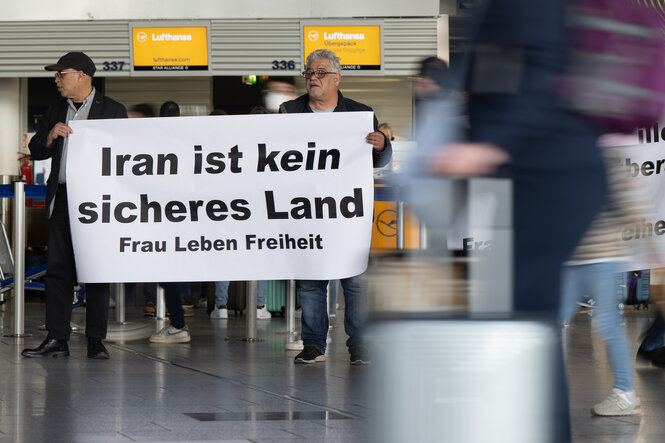 Zwei Männer halten ein Transparent vor einem Lufthansa-Schalter am Flughafen hoch