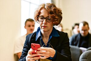 Eine Frau mit Locken und Brille guckt auf ihr rotes Handy