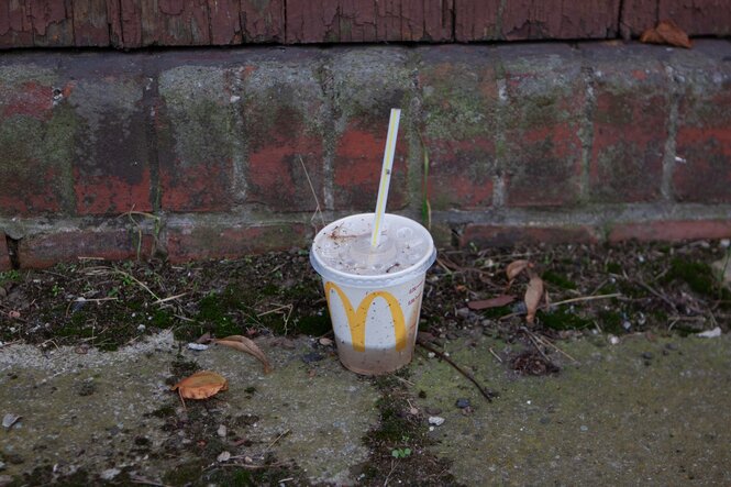 Ein Plastikbecher von McDonalds steht auf dem Asphalt