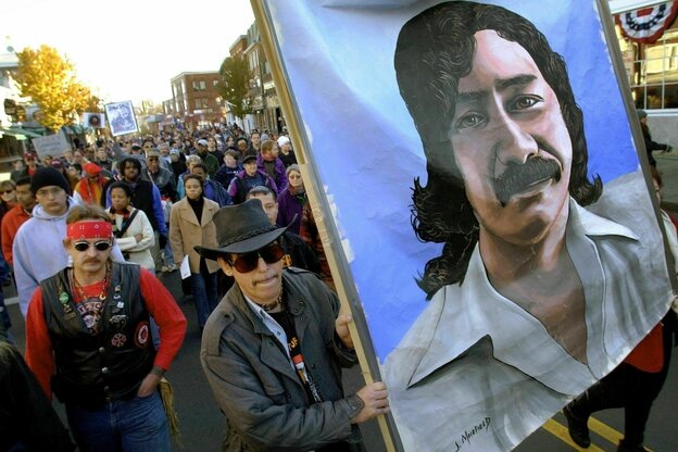 Menschen demonstrieren mit einem Plakat, auf dem das portrait von Leonard Peltier zu sehen ist