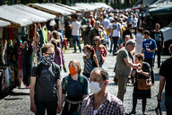 Menschen gehen mit bunten Masken über einen Wochenmarkt