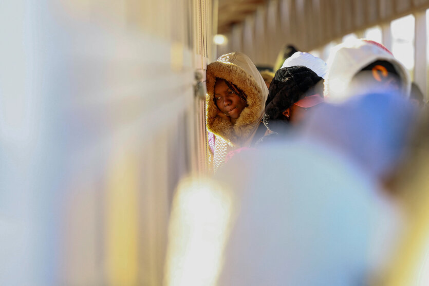 Eine Frau steht wartend in einer Menschenmenge und lehnt ihren Kopf an eine Wand