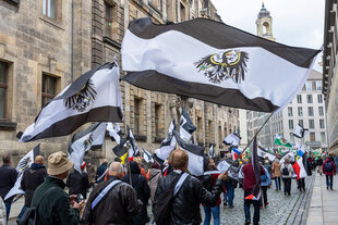 Menschen demonstrieren mit großen schwarz-weißen Flaggen mit einem Reichsbürger-Adler darauf in Dresden.