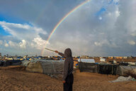 Eine Person deutet auf einen Regenbogen, im Hintergrund viele Zelte.