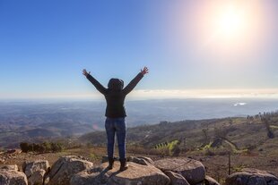 Eine Frau steht auf einem Berg und streckt die Arme in die Luft