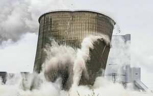 Der Kühlturm eines ehemaligen Kohlekraftwerks fällt in sich zusammen, es entsteht der Eindruck das der Turm noch raucht.