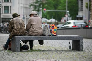 Zwei Menschen, die offensichtlich keinen festen Wohnsitz haben, unterhalten sich auf einer Sitzbank in der Innenstadt.