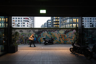 Ein Mann an dem Teil der Berliner Mauer entlang, der nun die East-Side-Gallery ist, am Eingang eines Neubau vorbei