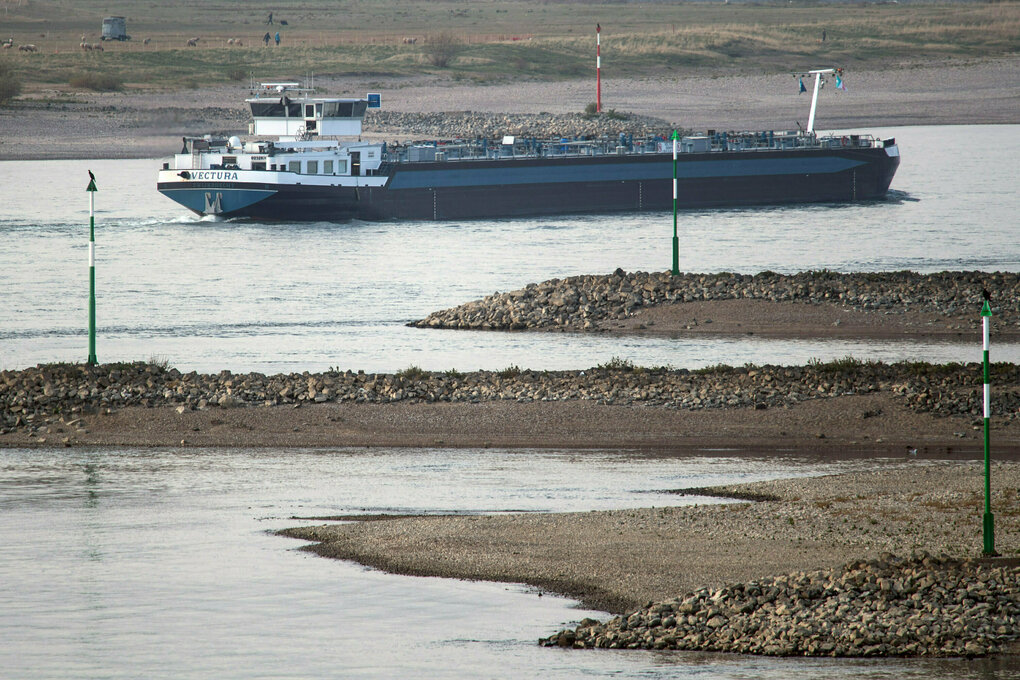 Schifffahrtszeichen stehen vollends im trockenen während ein Tankschiff durch die fahrrinne stampft.