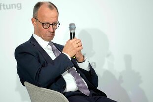 Friedrich merz hält ein Mikrofon in den Händen und schaut nachdenklich