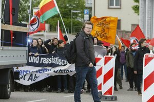 Michael Brandt im Vordergrund, hinter ihm eine Antifa Demo mit entspechenden Flaggen inklusive Kurdistan Flagge.