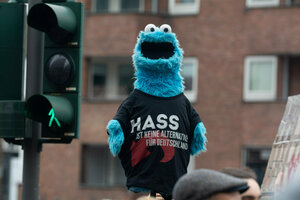 Ein Demo-Plakat besteht aus einer hellblauen Krümelmonster-Figur, das ein T-Shirt mit der Aufschrift 