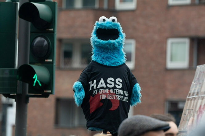 Ein Demo-Plakat besteht aus einer hellblauen Krümelmonster-Figur, das ein T-Shirt mit der Aufschrift "Hass ist keine Alternative" trägt