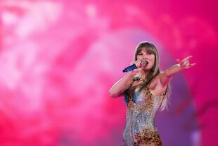 Taylor Swift auf der Bühne. Sie singt in ein Mikro und zeigt mit dem Finger Richtung Publikum.