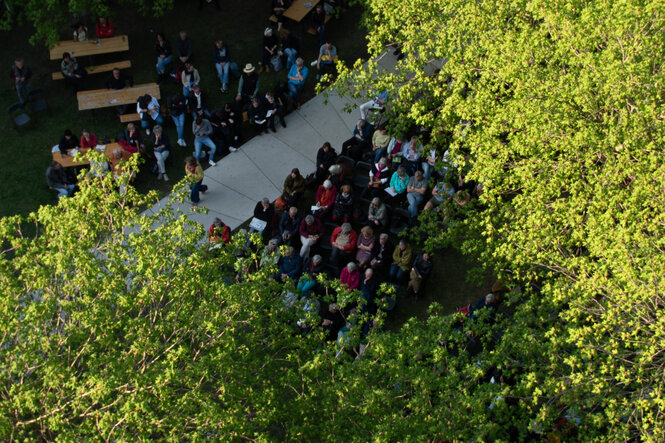 Das taz lab 2023 von oben. Neben Bäumen des Besselparks sitzen viele Menschen und schauen auf eine Leinwand.