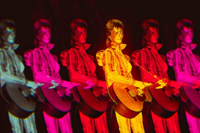 Filmstill: Eine Aufnahme von David Bowie bei einem Konzert ist multipliziert und abwechselnd in Grün- Pink-, Rot- und Orangetönen getaucht. Er spielt Gitarre und trägt ein schimmerndes Outfit mit Stehkragen.