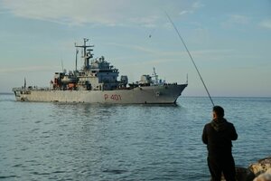 Ein Angler blickt auf das Meer, am Horizont ist ein Militärschiff