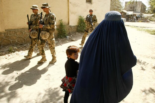 Bundeswehrsoldaten patroulieren auf einem Weg, in Gegenrichtung laufen eine voll schleierte Person und ein Kind