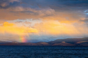 Die Strahlen der Sonne brechen sich in einem Regenbogenn über einem Bergsee