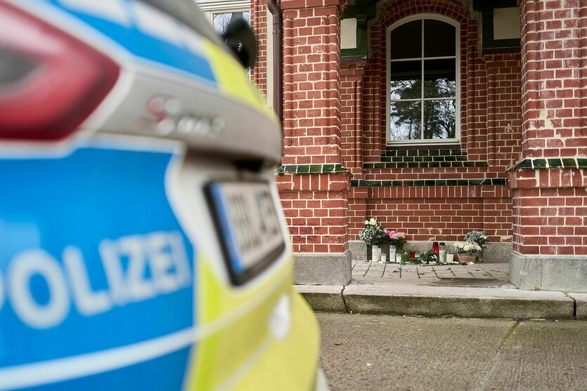 Blumen und Kerzen stehen vor dem Eingang eines Hauses nach einem Gewaltverbrechen, vor dem ein Polizeifahrzeug steht