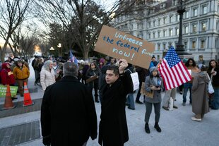 Protestierende gegen das Einfrieren der Leistungen mit Schildern und USA-Flaggen