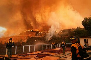 Flammen über Landschaft, davor Feuerwehrleute