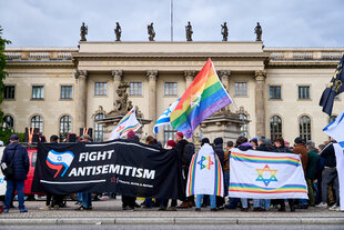 Eine Gruppe von Demonstranten steht mit Regenbogenflagge, Bannern die den Davidstern in Regenbogenfarben zeigen und ein Banner mit der Inschrift: Fight Antisemitism vor der Humboldt Universität