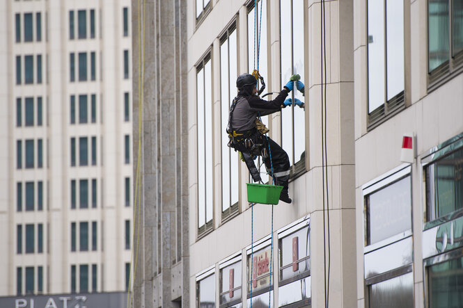 Ein Industriekletterer hängt an einem Seil und putzt die Fenster eines Geschäftshauses