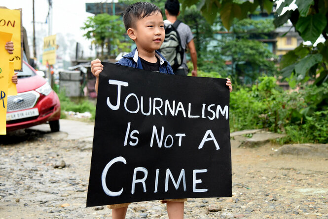 Ein Kind in Indien hält ein Transparent auf dem steht "Journalism is not a crime"