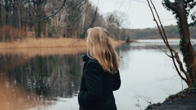 Eine Frau mit blondem langem Haar steht an einem See