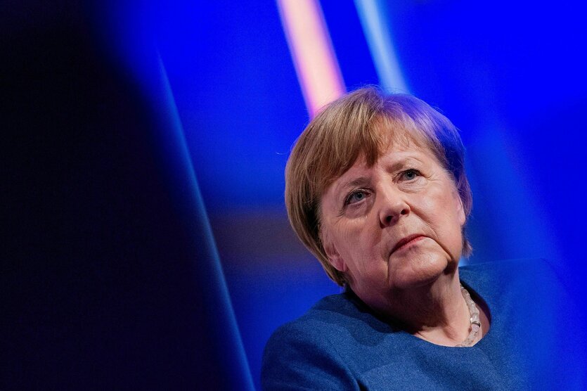 Angela Merkel schaut sehr enrst - die Umgebung ist blau in einem Veranstaltungsraum