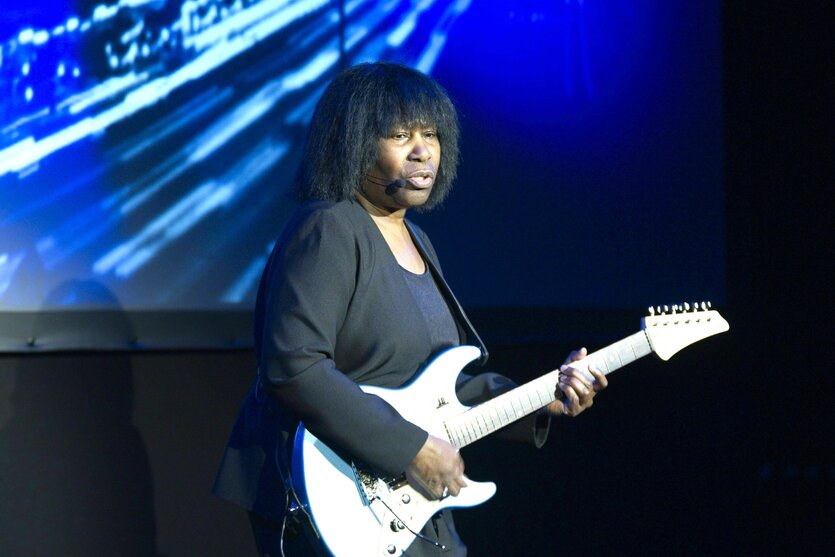 Joan Armatrading steht auf eine Bühne und spielt auf einer weißen E-Gitarre