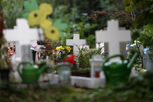 Windspiele, Blumen und Spielzeuge schmücken Kindergräber auf einem Friedhof.