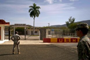 Ein Armeesoldat (r) und ein Marinesoldat vor den Toren, die die kubanische Seite von der US-Marinebasis Guantanamo Bay trennen - Eine Palme ragt in den blauen Himmel