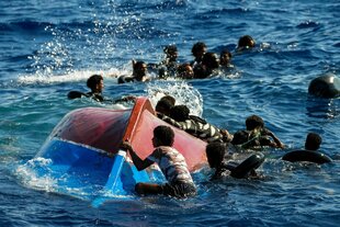 Afrikanische Migranten schwimmen neben ihrem umggstürzten Holzboot