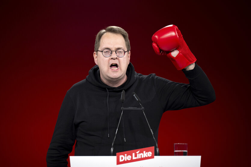 Sören Pellmann steht hinter einem Rednerpult und trägt einen linken Boxhandschuh, den er mit seinem Arm in die Höhe reckt