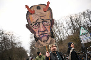 Demonstrant mit Plakat, das Merz als Teufel zeigt