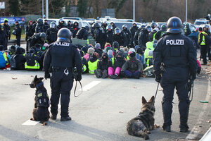 Sitzende Demonstranten umringt von Polizist:innen. Zwei Beamte führen Polizeihunde mit sich