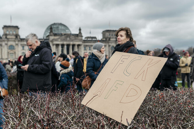 Protestmarsch gegen den Rechtsextremismus in Berlin Blick auf den Deutschen Bundestag mit einem Plakat mit der Aufschrift FCK AFD im Vordergrund