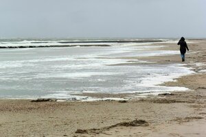 Eine Spaziergängerin geht an der mit Meeresschaum bedeckten Wasserkante am Südbad auf der ostfriesischen Insel