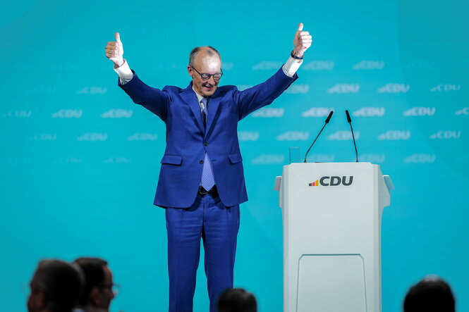 Friedrich Merz steht auf einer Bühne und winkt mit zwei Daumen nach oben ins Publikum.