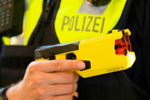 Ein Polizist in gelber Weste hält einen gelben, pistolenähnlichen Gegenstand mit vier Mündungen, darauf steht 